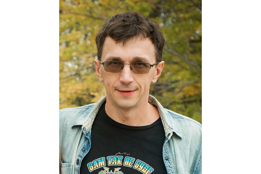 Andriy Prymak smiling at the camera wearing an eyeglass in front of a tree.