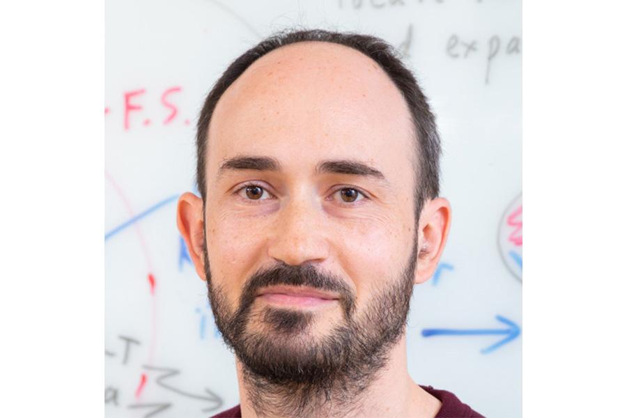 Gilles Ferrand smiling at the camera in front of a white board with equations.