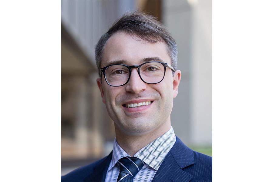 Richard Mikael Slevinsky wearing a blue coat and tie and wearing an eyeglass smiling at the camera.