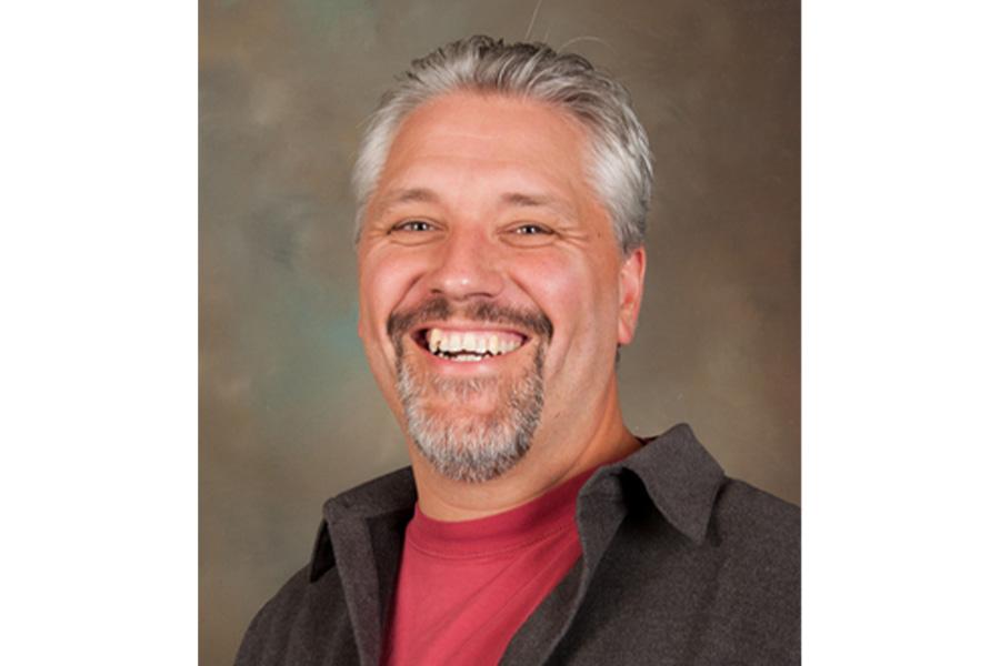 Alexandre Leblanc wearing a red shirt and coat smiling at the camera.