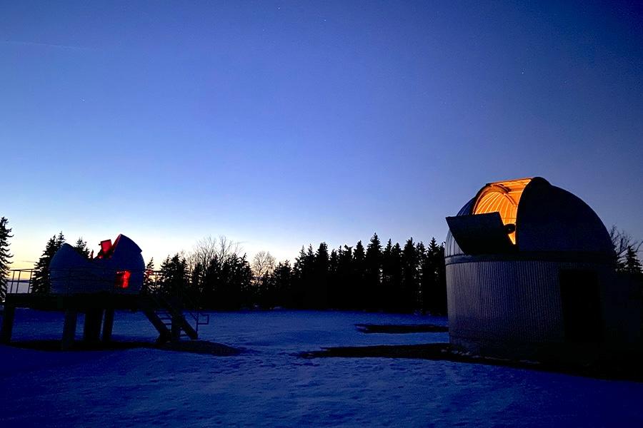 Glenlea observatory with the pine trees in the back and dark blue sky.