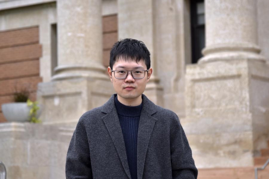 Xiaoke Qin wearing a black shirt and black coat with eyeglasses smiling at the camera.