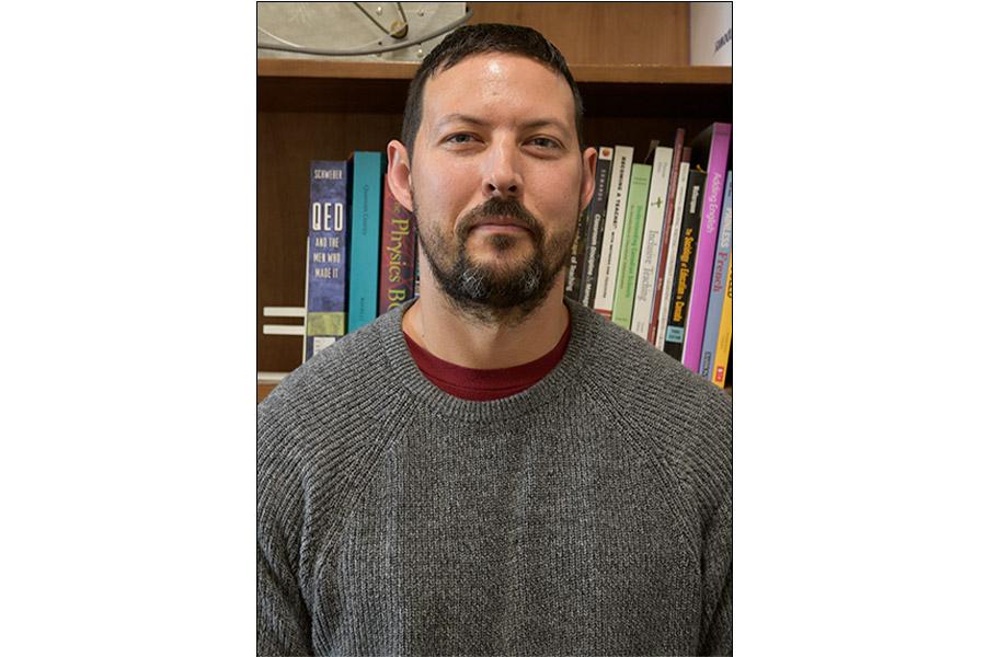Kyle Shiells wearing a gray sweater and smiling at the camera.
