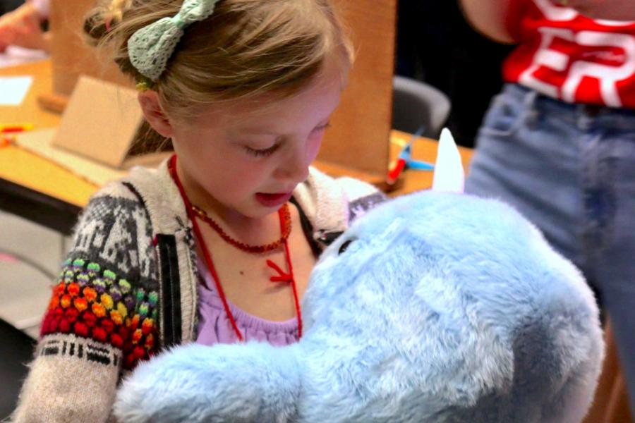 A kid hugging and looking at a robot plush.