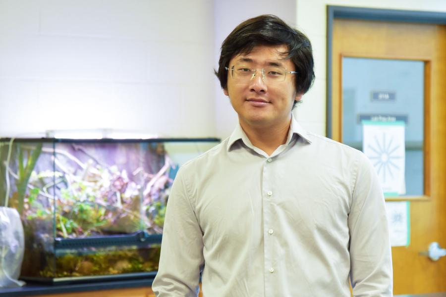 Kevin Pan wearing a light gray button down shirt and eyeglass smiling at the camera.