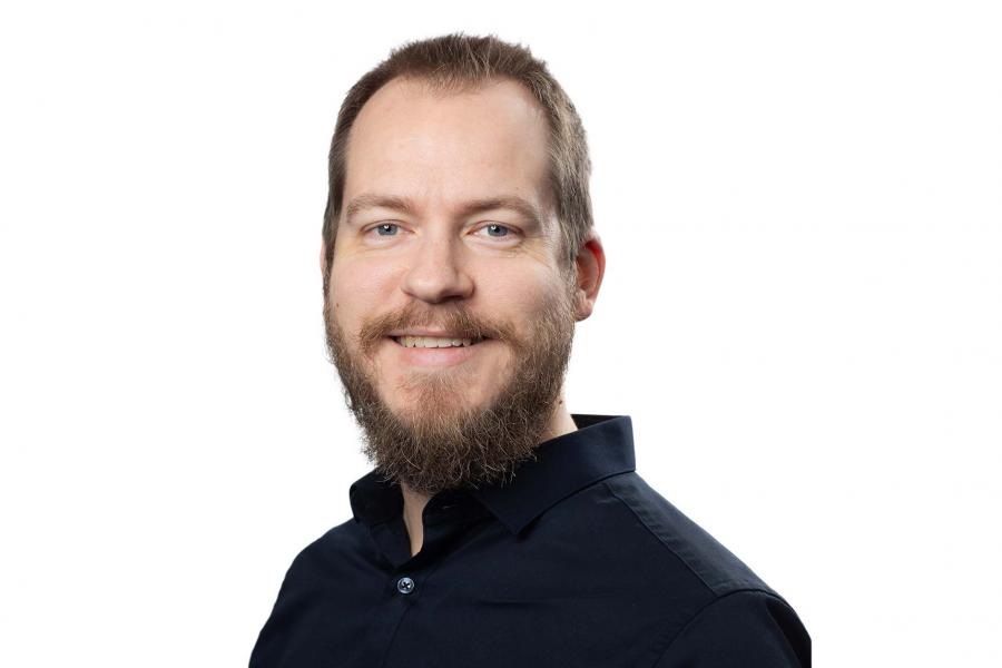 Olivier Tremblay-Savard wearing a dark button down shirt smiling at the camera.