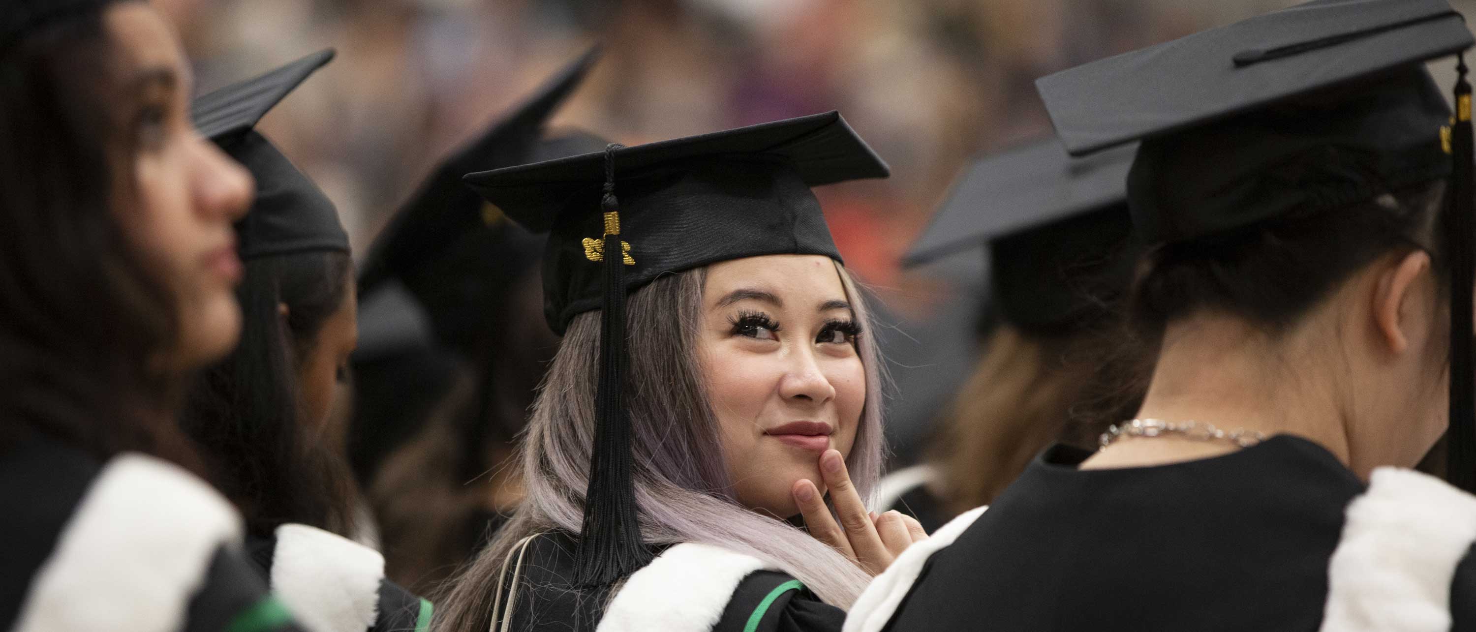 A close-up of a graduate wearing a cap and gown seated during the ceremony and looking over their shoulder.