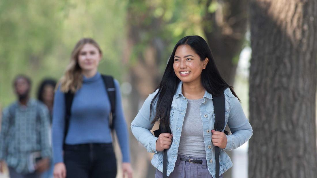 Smiling students walk on campus wearing backpacks.