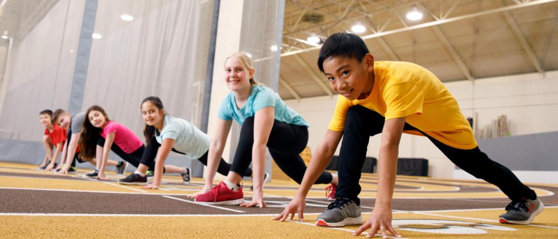 Six junior program track and field participants ready at the starting line.