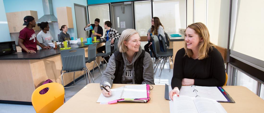 Several small groups of students study, eat and socialize in a common lounge area of a student residence.