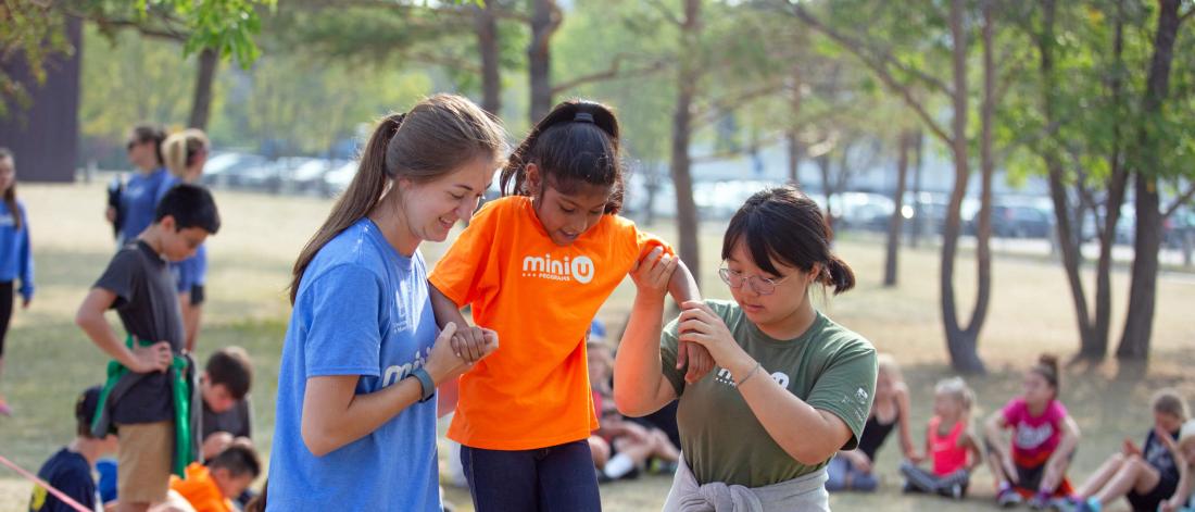 A Mini U child carefully walks along a slackline with the help of two Mini U leaders.