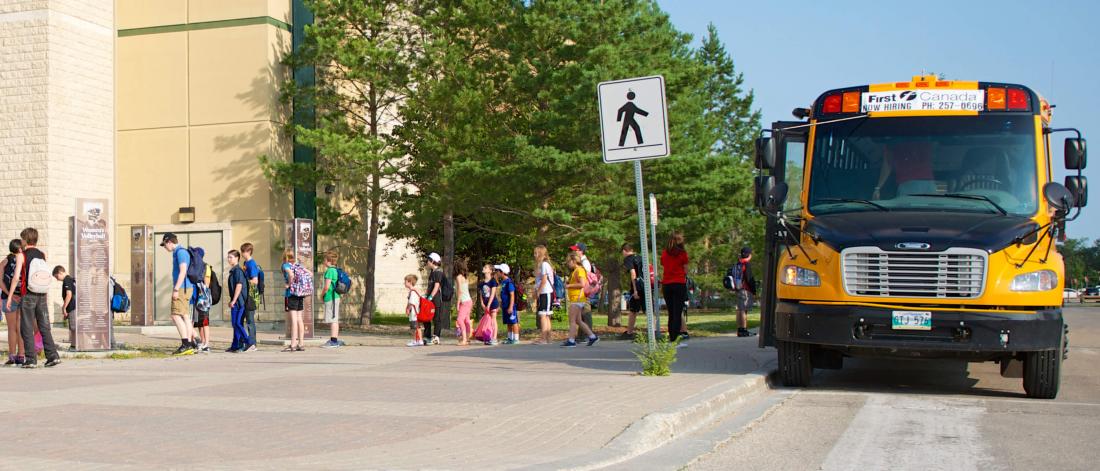 A school bus is parked at a crosswalk as a line of children exit the bus.