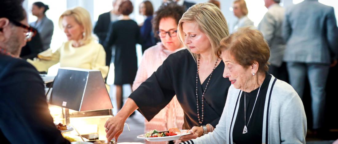 Several people serve themselves food at a buffet line during an event.