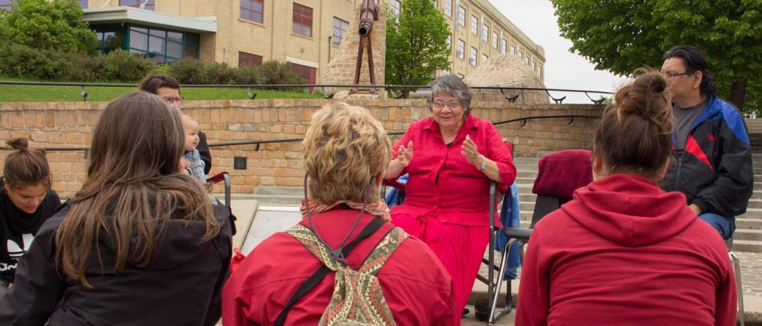 A crowd of people mostly dressed in red gather in a circle while a woman speaks.