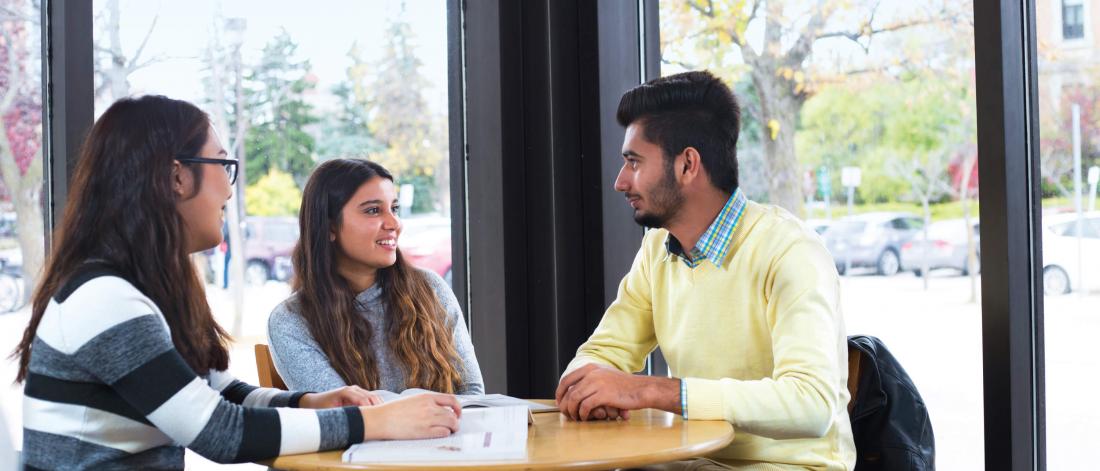 Three students sit at a table together talking.