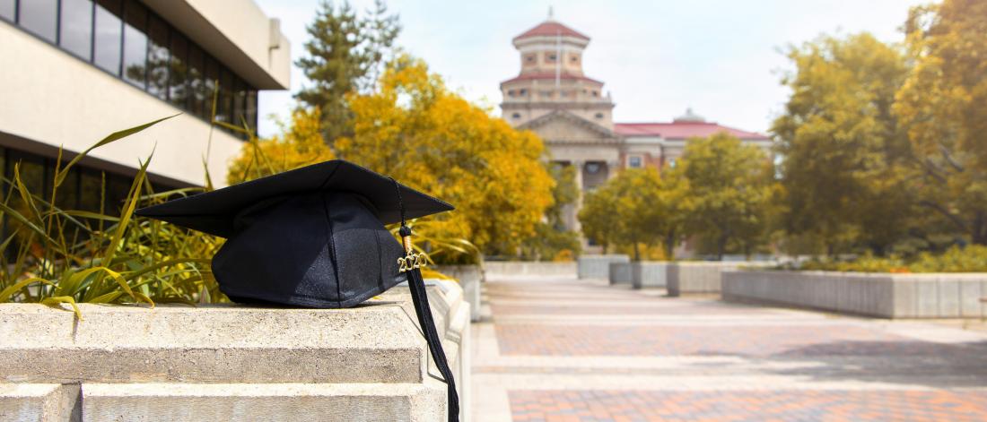 A cap and tassel sit in front of the Admin building on a fall day.