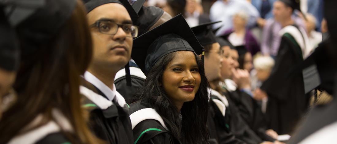 A graduate smiles at the camera at her convocation ceremony in line with several others.