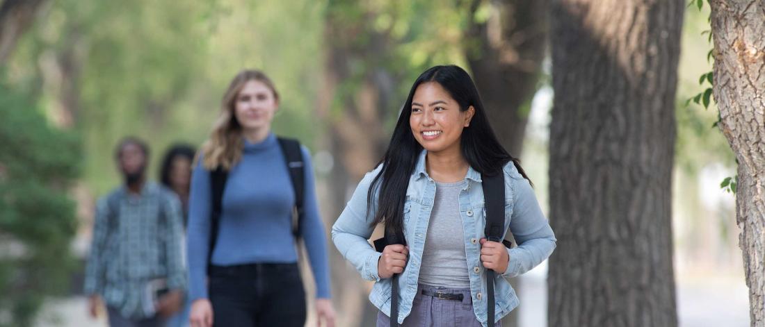 Smiling students walk on campus wearing backpacks.