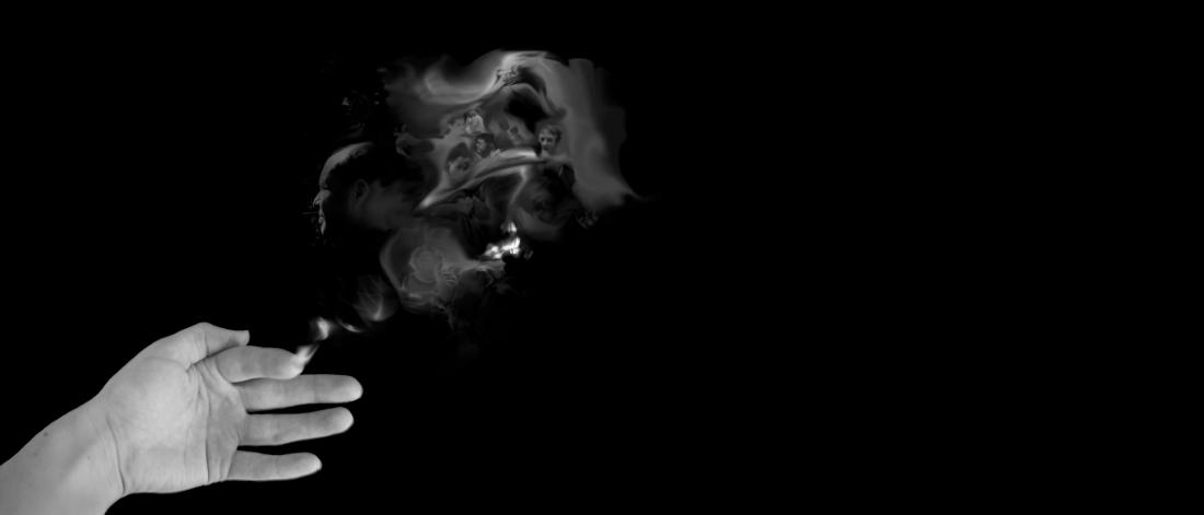 Edited black and white photo showing an open hand with smoke descending from the top of the index finger. Inside the smoke are faint images of different people's faces.
