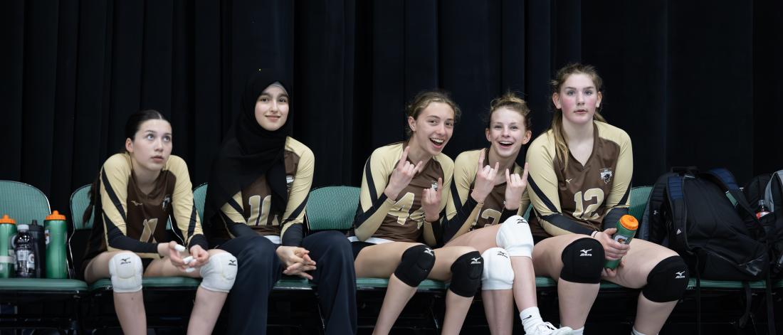 Junior bisons girls sit smiling together on the bench