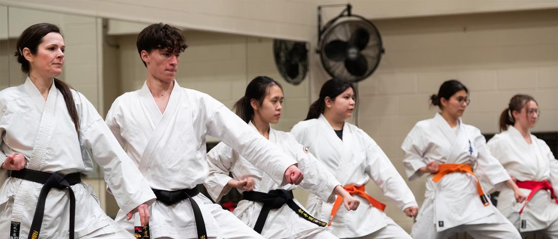 a group of karate students stand in a low block position side-by-side