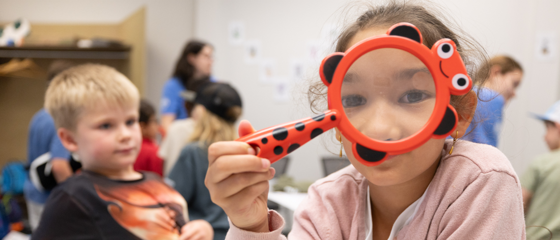 A mini u camper holding a magnifying glass up to their eye