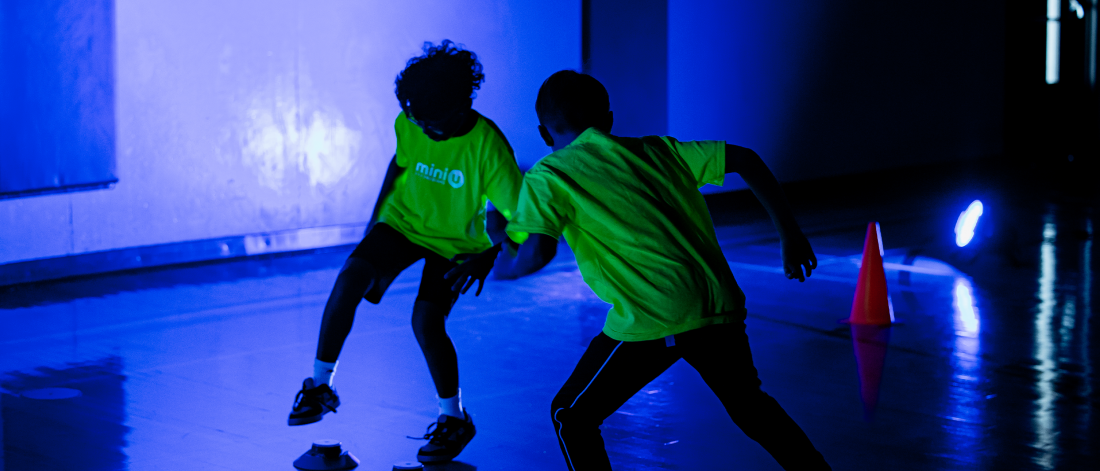 Two mini u campers running in the glow and the dark shirts during an activity in a gym