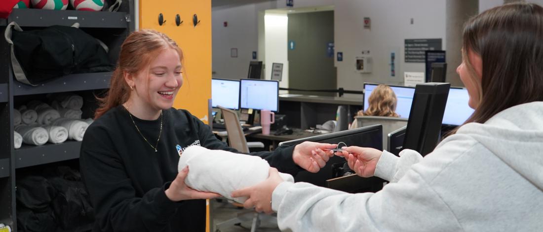 Gym user exchanging ID card for towel with customer service staff. Both are smiling.