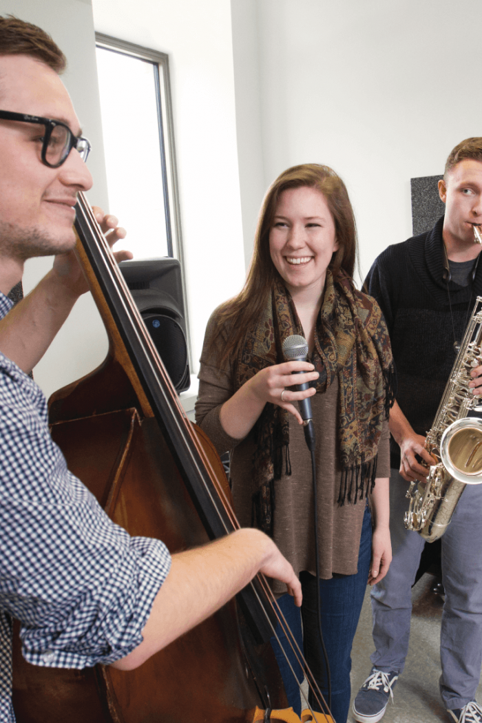 Three students practice their instruments together in a small practice room. 