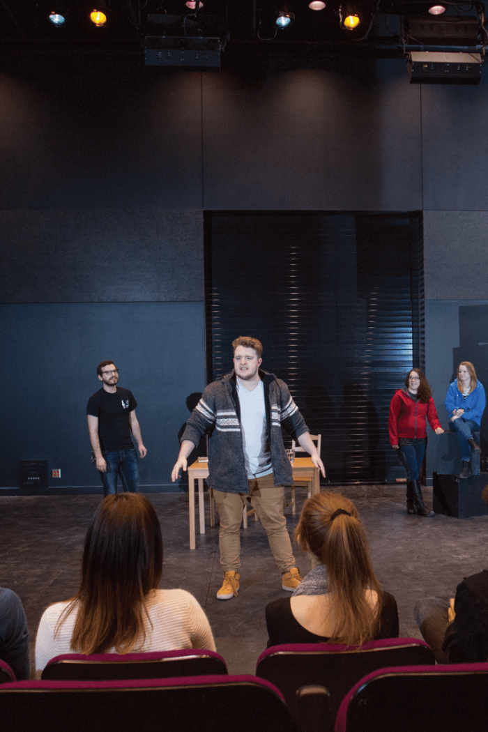 A small group of students performs on stage for an audience seated in a theatre.