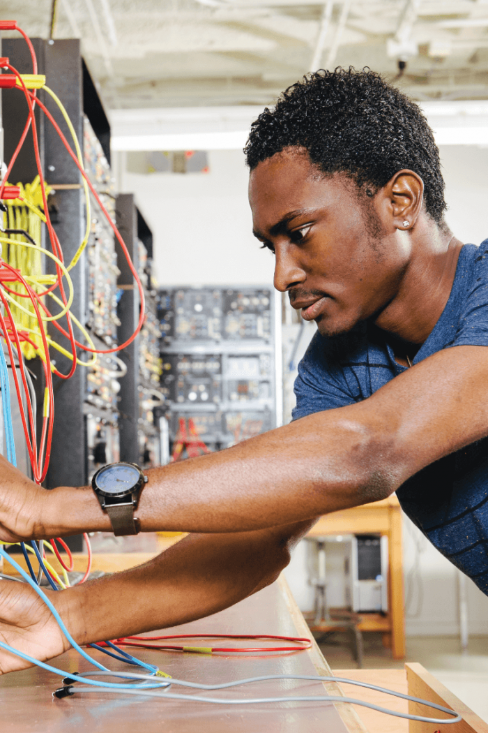 A student works at a desk connecting wires to a console. 