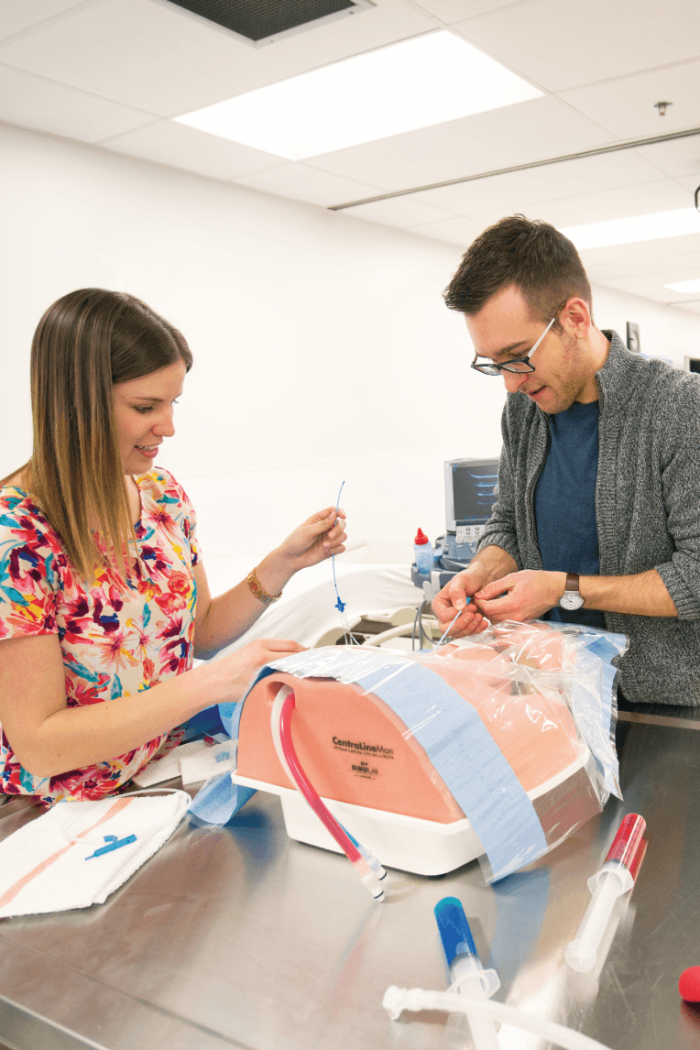 Two students practice setting an intravenous line on a mannequin. 