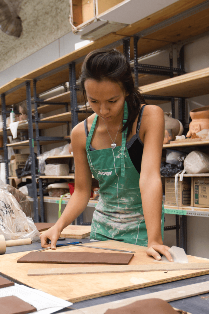 A student stands at a counter working on a clay project.