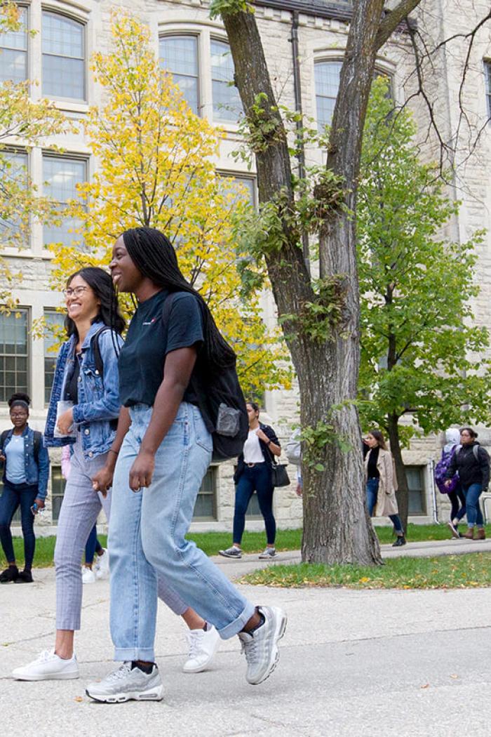 Students walk near the Tier Building through full, autumn trees. 