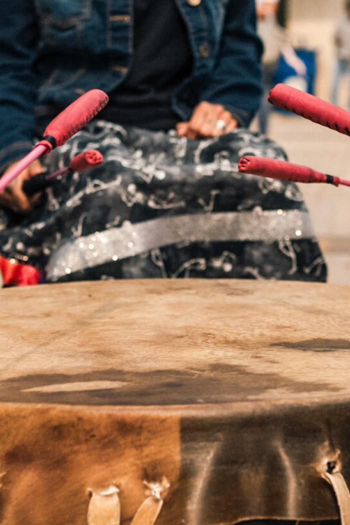 Hands holding drumsticks hitting an Indigenous drum.