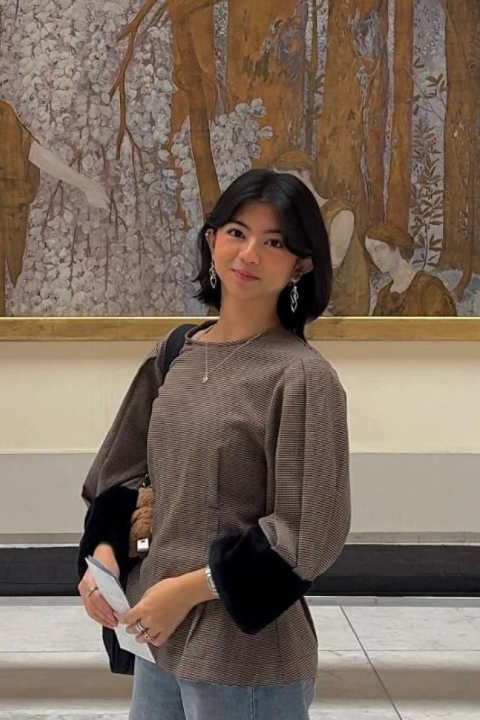 Justine, standing in front of a large painting smiling slightly at the camera.