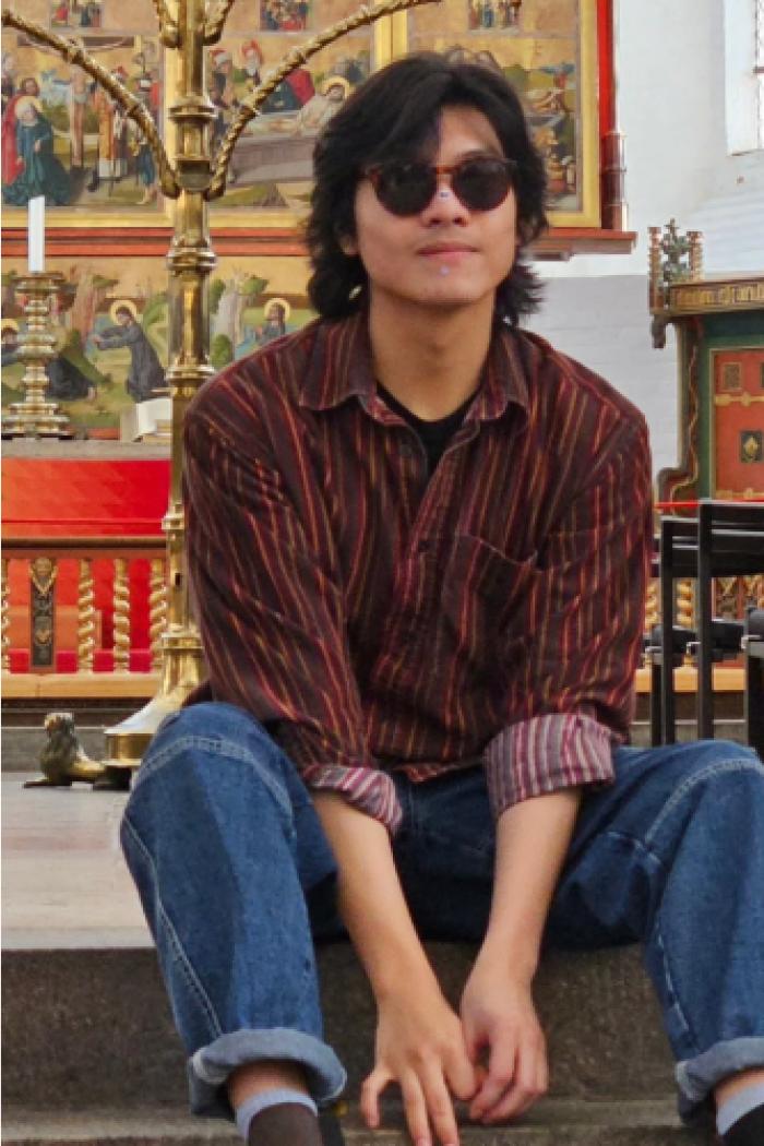 LJ, wearing sunglasses and sitting calmly in an indoor space.