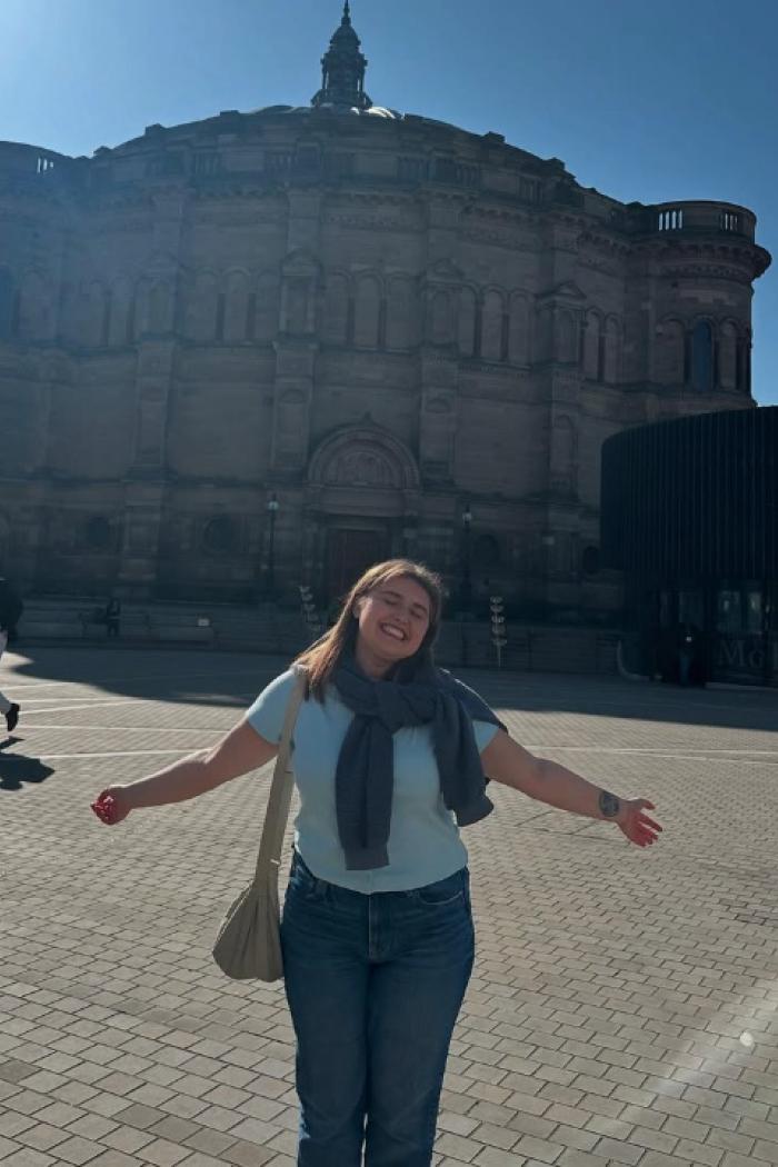 Morgan posing in front of a structure on a sunny day with both arms raised.