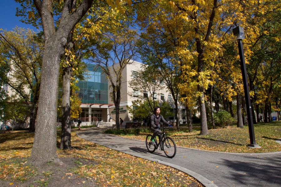 A University of Manitoba student on a bicycle outside the Helen Glass Centre of Nursing on a sunny autumn day