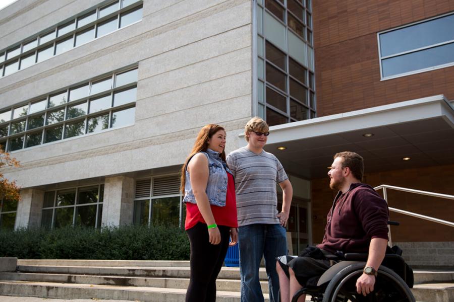 Two people standing talking to a third person in a wheelchair outside of a building at University of Manitoba