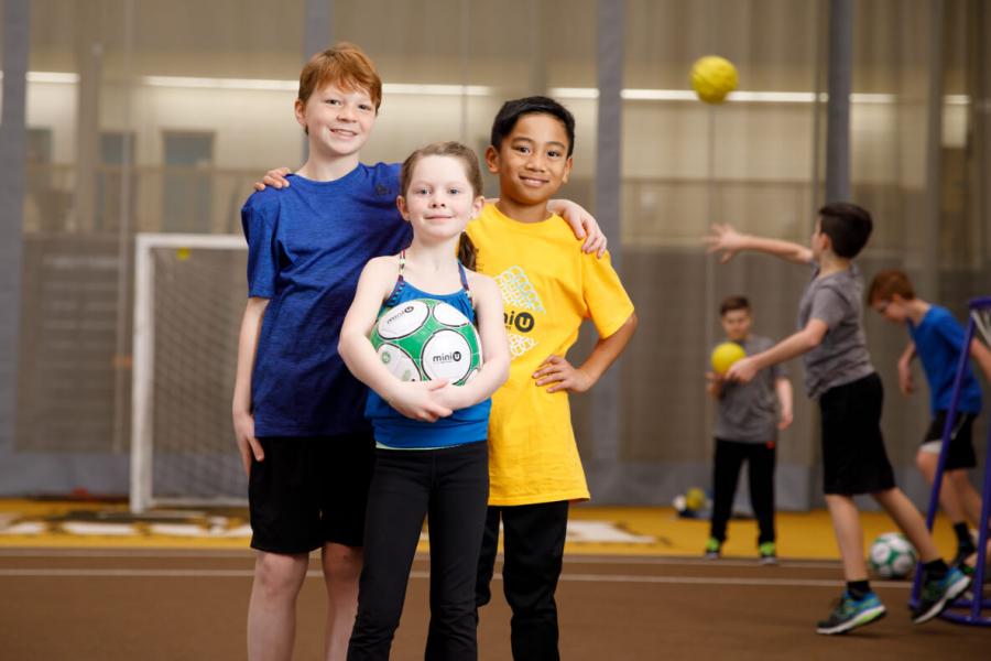 Three kids holding a soccer ball during the Mini U program
