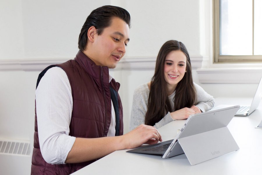 Two University of Manitoba students happily sit together at a desk looking at a laptop.