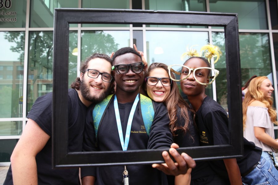 Four students pose for a funny photo holding a photo frame and wearing fun costume props.