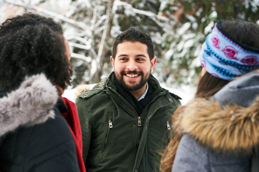 Three international students in parkas chat outside in winter.