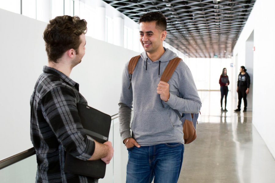 An international graduate student chats with a mentor in a UM hallway. 