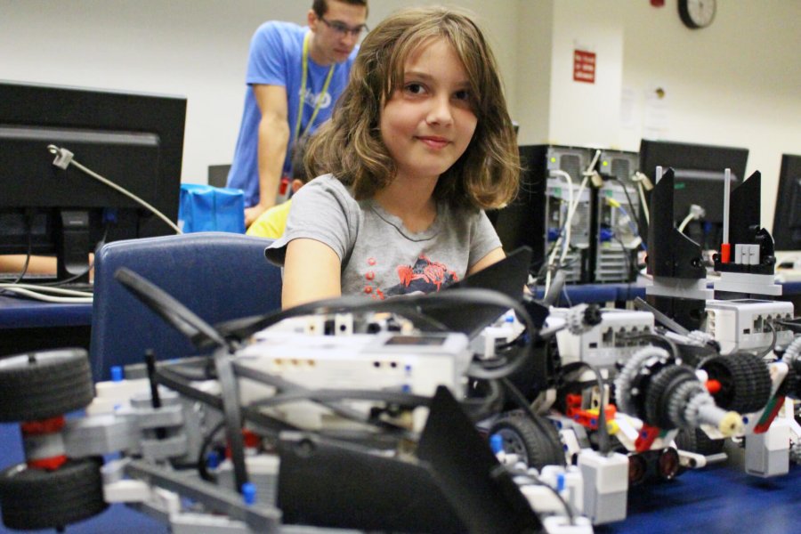 A child sits at a desk surrounded by robotics in a computer lab.