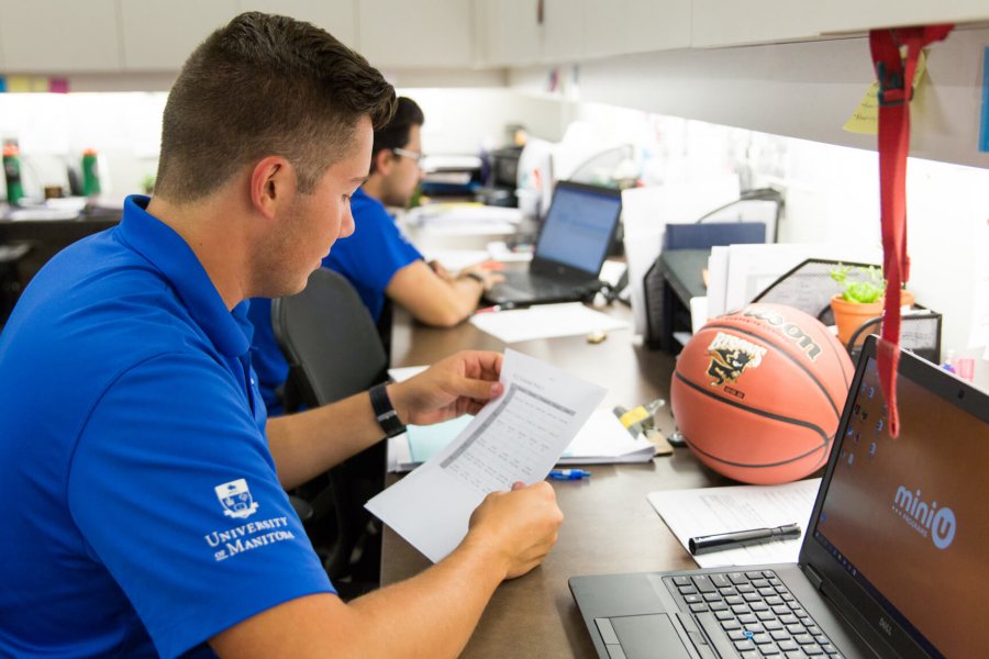 Two Mini U leaders fill out paper work in an office in front of laptops.