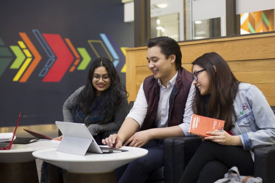 Three students sitting together looking at a laptop monitor while studying in a lounge area.