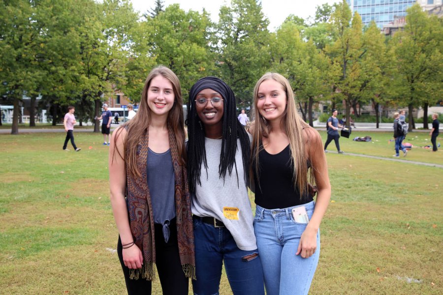 Three students stand beside each other and smile for the camera while standing in the Fort Garry campus Duckworth Quadrangle.