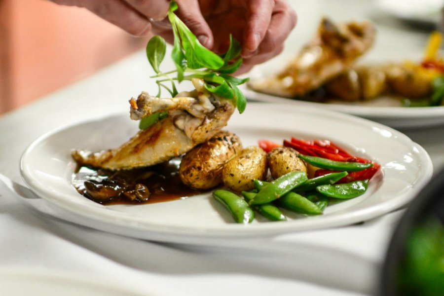 A pair of skilled hands carefully place the garnish on top of a plated meal. 